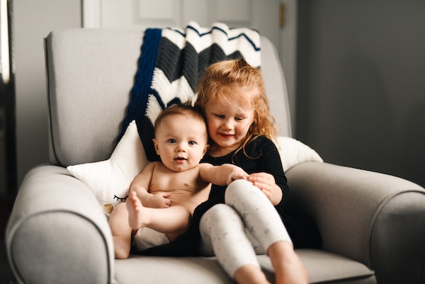 A small child sitting with and embracing their younger sibling